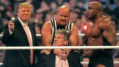 Getty Images Donald Trump, in suit and tie, shows off a trimmer as Stone Cold Steve Austin, in a sleeveless referee shirt, restrains an irate Vince McMahon