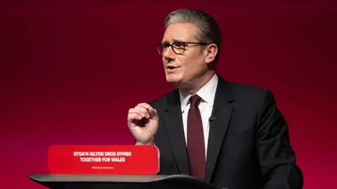 Getty Images UK Prime Minister Sir Keir Starmer speaks at a lectern in front of a red Labour background.