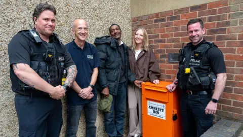 Northamptonshire Police A group of four men and a woman pose for a picture beside an orange knife amnesty bin.