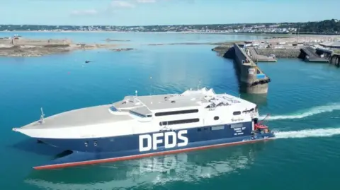 A picture of a large blue body of water with part of the harbour visible. There is a large white and blue boat with DFDS written on its side.
