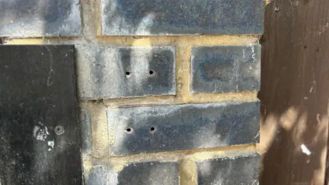 A grey wall outside a home with holes in the wall where a lockbox used to be
