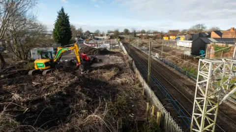 An ariel shot of a yellow digger at the side of a blue train track.