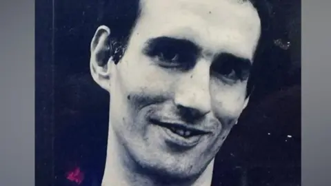 Family A black-and-white close-up portrait of Antony Irvin with short dark hair, slight stubble and a faint smile, facing slightly to one side.