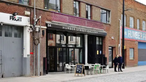 Bernard Sharp / Geograph Exterior view of the glass-fronted Humber Street Gallery with tables and chairs outside on the pavement