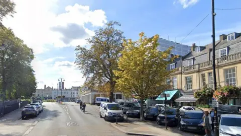 Montpellier Walk on a sunny day with lots of parked cars on the right, a few restaurants to the right and some trees