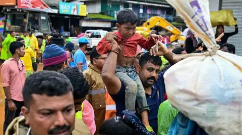 Getty Images Rescue personnel escort tea plantation workers to the relief camps, after landslides in Wayanad on July 31, 2024.