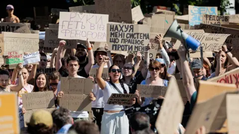 A group of Ukrainians protest. They are holding up signs with Cyrillic written on them.