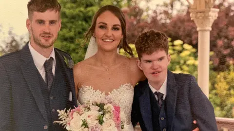 Family photo of a wedding with Fraser standing next to the bride. He is wearing a smart wedding suit