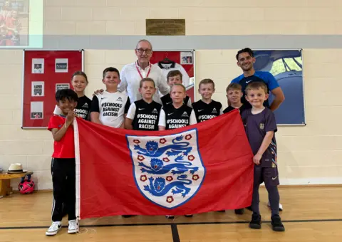 George King/BBC News Terry Butcher with young students and a large red England flag with the Three Lions badge on 