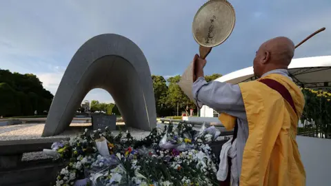 Getty Images Back view of a monk in a yellow robe standing in front of a memorial statue