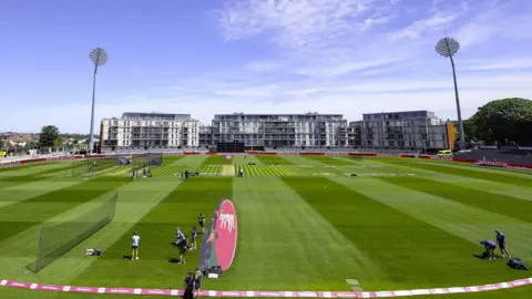 A wide shot of the Seat Unique cricket stadium in Bristol, with flats and high-rise buildings in the background, as a training session takes place on the pitch