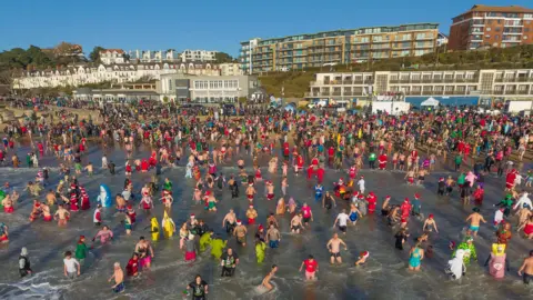 Steve Hogan Photography A picture of people running into the sea as part of the swim with buildings on the shore towering over the beach.