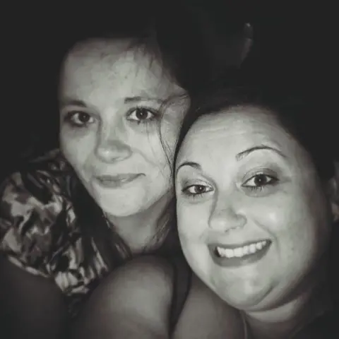 Elli Wood A black-and-white selfie-style photo showing the heads and shoulders of two smiling women whose faces are touching