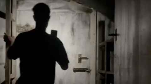 A silhouetted man standing in front of a bolted door 
