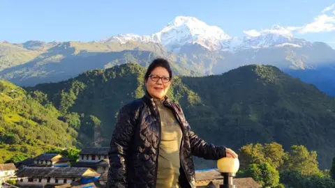 Happy Chhetri Happy Chhetri, one of the pioneering women trekking guides in Nepal, poses in front of the Himalayas which can be clearly seen