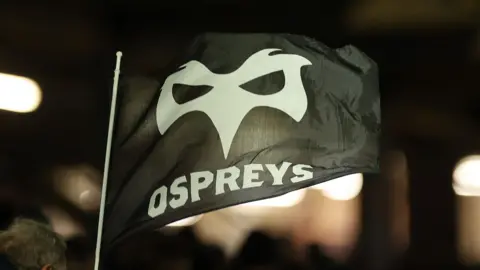 An Ospeys flag flutters in the breeze at a game