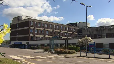 BBC A view of the outside of North Devon District Hospital. It is a multi-storey brick building with a white entrance.