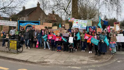 A group of children and adults stood outside a school holding placards and flags