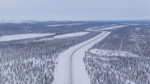 Getty Images An aerial view of an icy and snowy road running through miles of forest