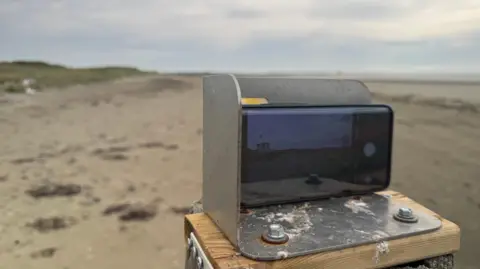 A metal phone holder on top of a post on a beach.