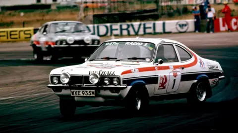 LAT Images/Getty Images A colour photo of a modified 1970s saloon car on a racing circuit. It is mostly white but decorated with various decals including the figure '1' and logos for Vauxhall and Goodyear, as well as having the name of BBC Radio 1 and the station's frequency, '246m', written across the top of the windscreen.