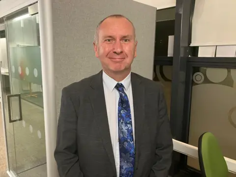 A picture of Pyramid Trust CEO Steve Kelly in a dark grey jacket with a blue tie with flowers on it.