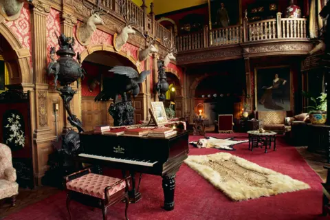 Getty Images The image shows a large room inside the castle. There is a deep red carpet on the floor, a piano and stags' heads on a wall.