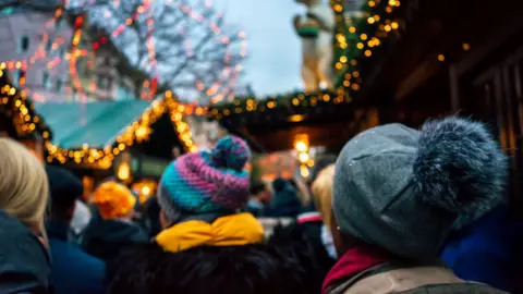 The back of people's head in bobble hats. They are at a Christmas fair.