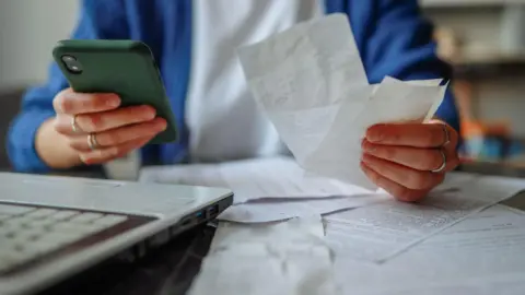 A stock image of someones hands holding receipts and a green phone.