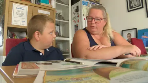 BBC News Tommy, 7, sitting at a table with books being home educated by his mother Rachel