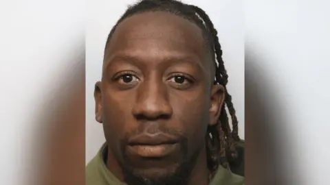 Wiltshire Police Shepherd Murombedzi looking at the camera in a police mugshot. He has long dreadlocks and is wearing a green top.