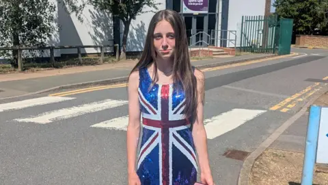 Stuart Field A 12-year-old girl is pictured outside her school wearing a sequined red, white and blue union jack dress and is looking sad at the camera.