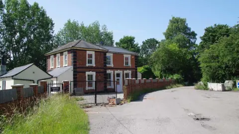 Glyn Baker/Geograph The station house when it had been renovated as a private property, with black metal gates. The road outside it is totally clear of rubbish.