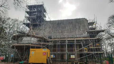 LDRS A chapel is covered in scaffolding with a yellow box at the front with a sign saying site office. It is winter, the trees behind the chapel have no leaves and the sky is grey.