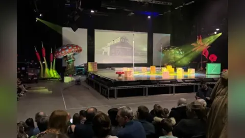 Keely Beecroft A stage with props. There are audiences watching the stage. 