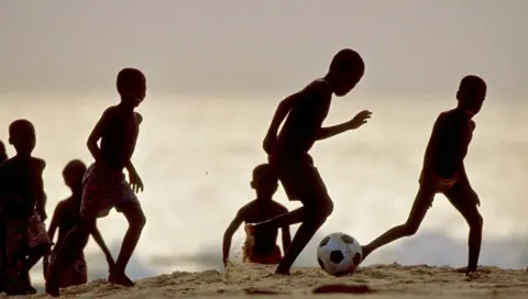 Getty Images Boys in Silhouette bermain sepak bola di pantai di Ghana.