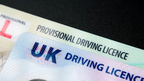 An extreme close up image showing the top of a full UK driving licence physical card sitting on top of a provisional driving licence physical card