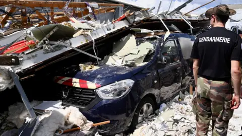 French gendarme looks at car crushed under collapsed building