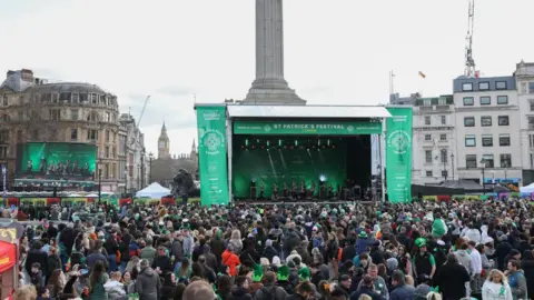 Getty Images A large crowd gathered in Trafalgar Square for the St Patrick’s Festival, featuring a main stage with green branding and Nelson's Column in the background.