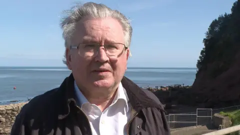 Cllr David Cox standing in front of the cliff fall at The Ness in Shaldon