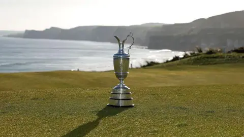 The Claret Jug sits on the 5th hole during media day for the The 153rd Open Championship at Royal Portrush Golf Club. Cliffs and the sea are in the background.