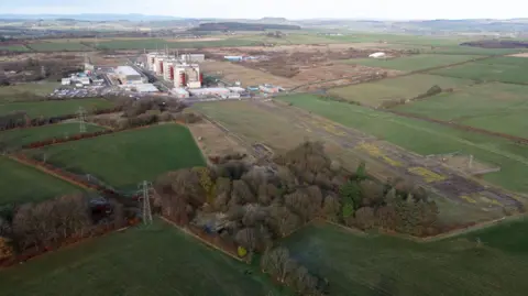 Green fields and trees surrounding the last buildings left on a former nuclear power station site in southern Scotland