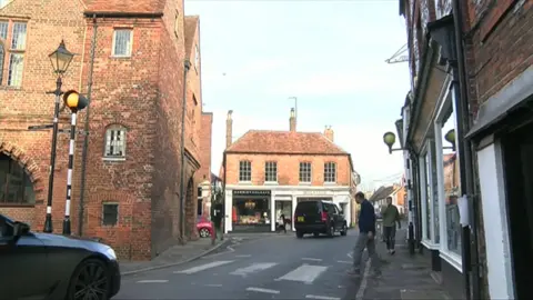 Watlington High Street. The road is narrow and there are tall red-brick buildings either side of the road.