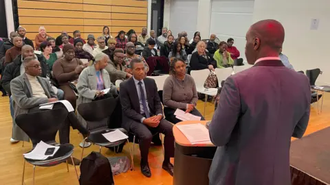 El reverendo Foster se encuentra en el podio y habla con los asistentes al evento de Nottingham.