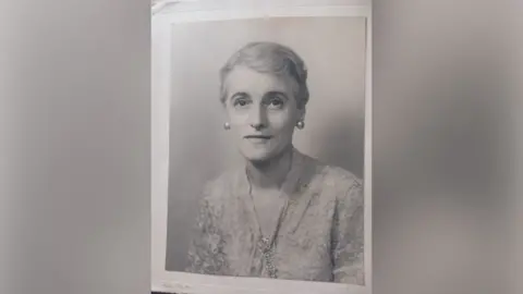 FAMILY PHOTO Lydia, to whom Stanley apologised in his postcard. It is a black and white photograph of an adult woman with her hair tied back. She is wearing a lace blouse and has chunky earrings on. 