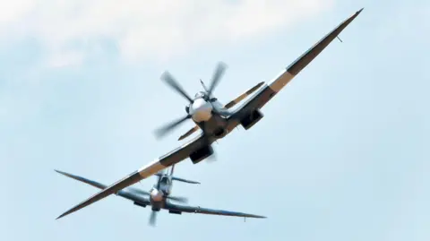 Two Spitfires fly in the sky.