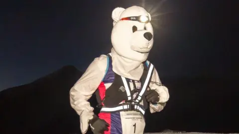 Gillian Punt A runner dressed as a polar bear with a head torch on is seen running in the dark. The runner has black gloves and a running vest over the top of the bear costume. 