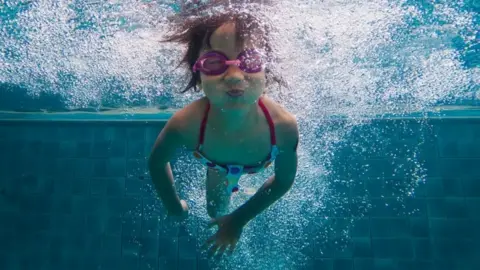 A child swims in a pool, under water and wearing googles.