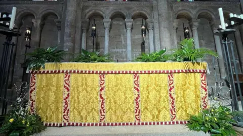 Peterborough Cathedral A green and yellow floral decoration around a ceremonial yellow and red cloth inside the Cathedral.