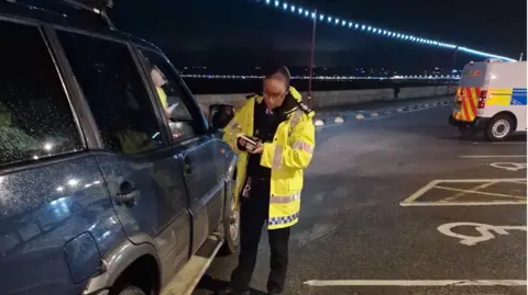 A picture of an officer completing a roadside test. The lady is wearing a green jacket.